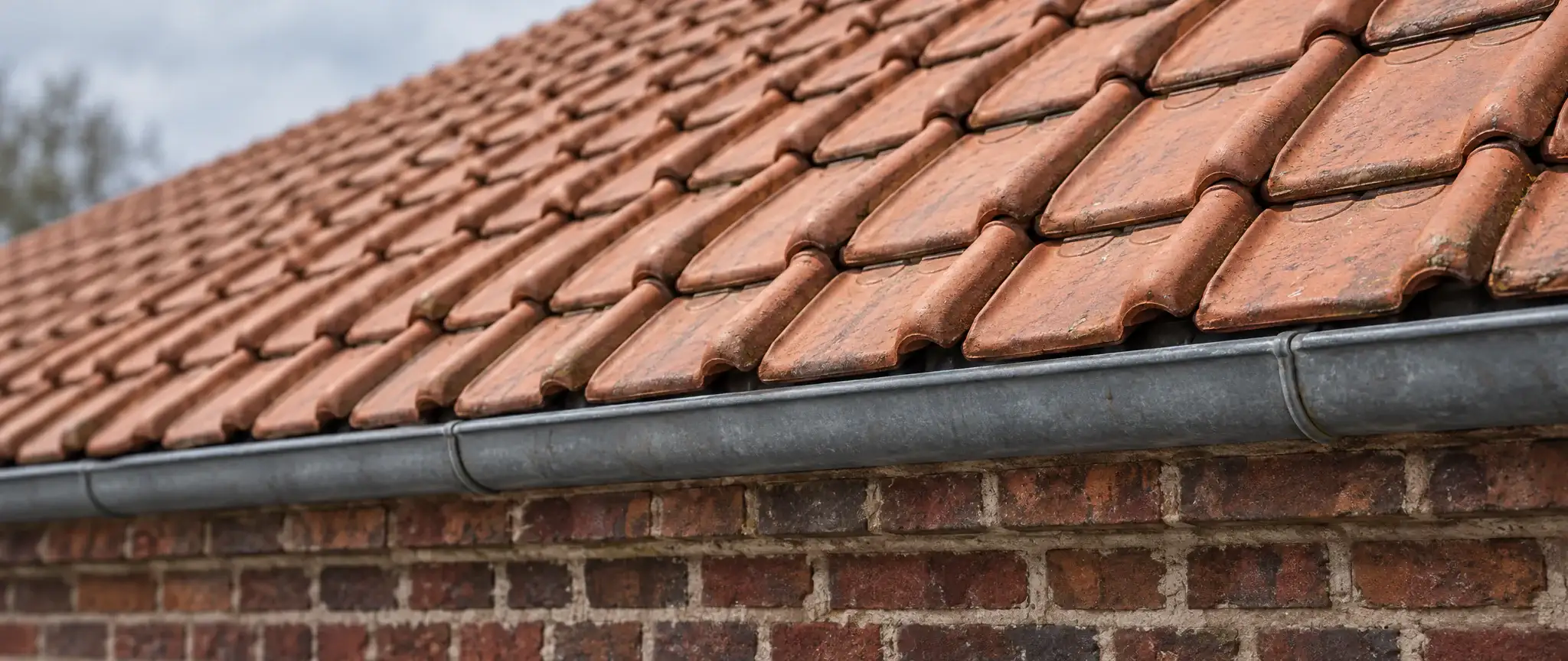 Couvreur à Dunkerque : rangs de tuiles en terre cuite au-dessus d’une gouttière en zinc et d’un mur en briques rouges